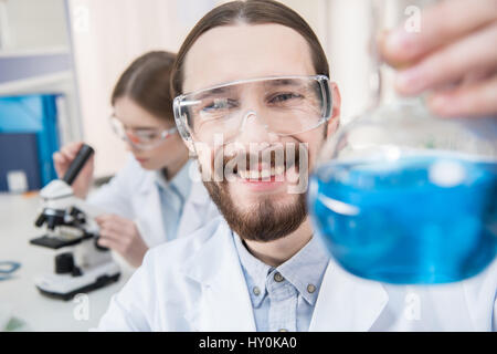 Sorridente giovane scienziato holding pallone con reagente chimico Foto Stock