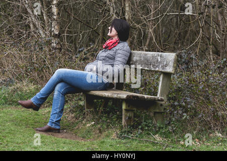 I giovani adulti pensando donna appoggiata sul banco di legno nel parco. Autunno freddo meteo. Raccolto orizzontale Foto Stock