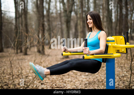 Ritratto di forte giovane donna appesa sul muro di barre con le gambe verso l'alto. Donna Fitness esecuzione di appendere solleva la gamba all'aperto. Foto Stock