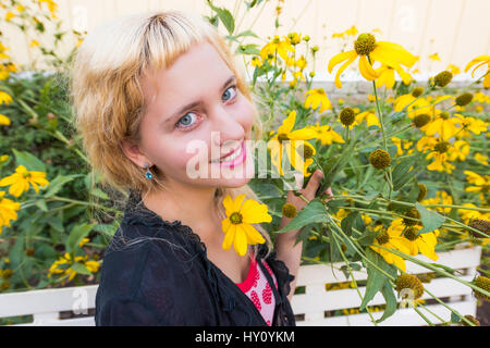 Primo piano della giovane donna sorridente da alte giallo girasole fiori a margherita sul banco di lavoro Foto Stock