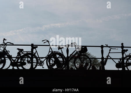 Silhouette di biciclette incatenati alle rotaie del ponte Foto Stock