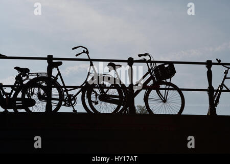 Silhouette di biciclette incatenati alle rotaie del ponte Foto Stock