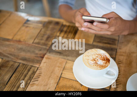 Elevato angolo di visione della donna utilizzando il telefono cellulare con la tazza di caffè sul tavolo al cafe Foto Stock