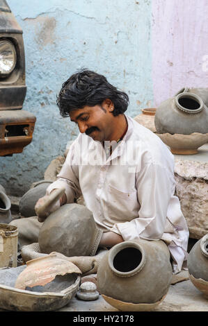 Un vasaio seduto sulla strada di Udaipur, usando una pala a forma pentole di creta Foto Stock