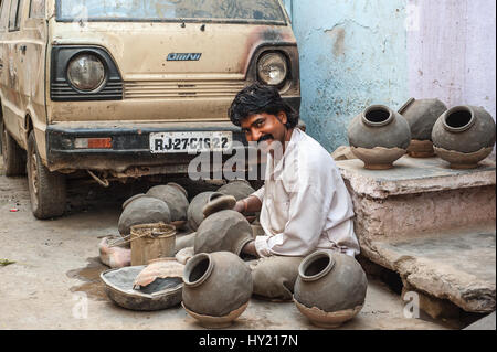 Un vasaio seduto sulla strada di Udaipur, usando una pala a forma pentole di creta Foto Stock