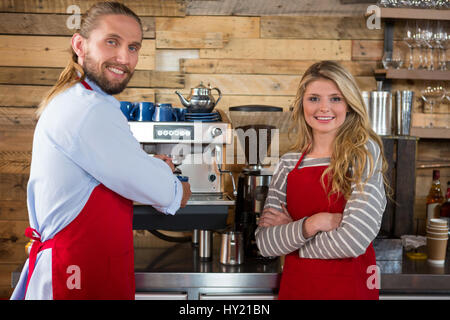 Ritratto di maschio e femmina baristi in piedi dalla macchina da caffè presso la caffetteria Foto Stock