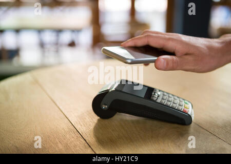 Immagine ritagliata della mano del cliente di pagare attraverso smart phone nel coffee shop Foto Stock