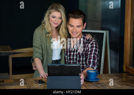 Sorridente coppia giovane utilizzando tablet PC al tavolo in coffee shop Foto Stock