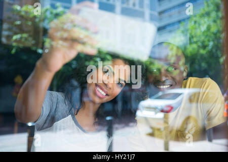 Sorridente coppia giovane tenendo selfie con cellulare in coffee shop visto attraverso la finestra Foto Stock