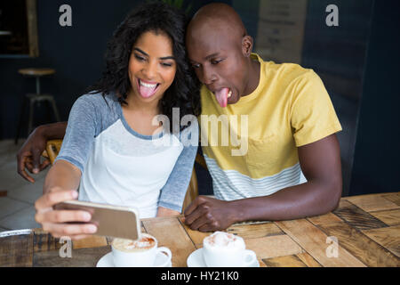 Giocoso giovane rendendo volti mentre prendendo selfie nel coffee shop Foto Stock