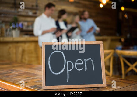 Aprire il cartello sulla tabella con i clienti in background a coffee shop Foto Stock