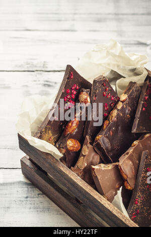 Varietà di barrette di cioccolato in una scatola di legno su luce sullo sfondo di legno Foto Stock