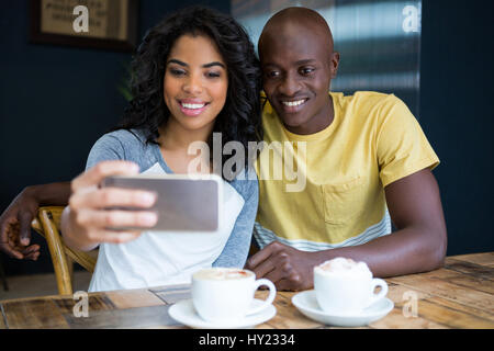 Sorridente coppia giovane tenendo selfie con cellulare in coffee shop Foto Stock