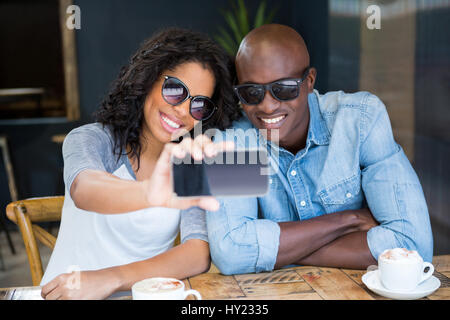 Sorridente coppia giovane tenendo selfie con smart phone nel coffee shop Foto Stock