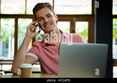 Bel giovane uomo che parla al telefono cellulare in cafe Foto Stock