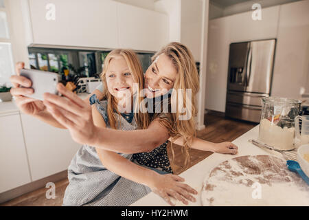 Carino bambina e la sua bella madre tenendo selfie sorridente e preparare l'impasto per la cottura in cucina. Felice famiglia giovane di madre e da Foto Stock
