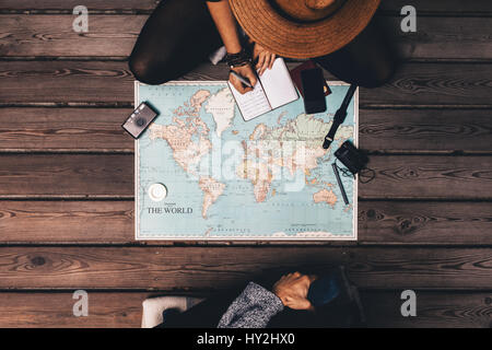 Uomo e donna vacanza di pianificazione utilizzando una mappa del mondo e altri accessori da viaggio. Donna rilevando i punti della discussione in un piccolo diario.
