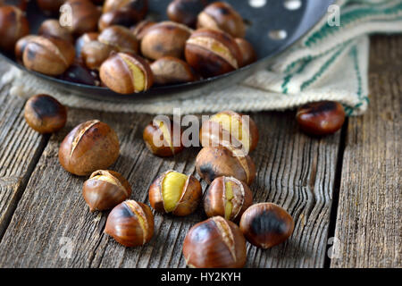 Castagne arrosto con un castagno forata Teglia su un vecchio tavolo di legno con biancheria vintage Foto Stock