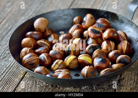 Castagne arrosto con un castagno forata Teglia su un vecchio tavolo in legno Foto Stock