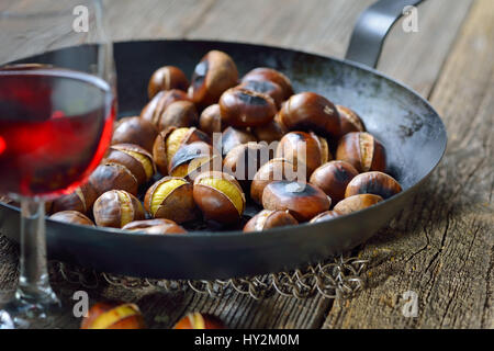 Castagne arrosto con un castagno forata Teglia su un vecchio tavolo in legno servito con un bicchiere di vino locale Foto Stock