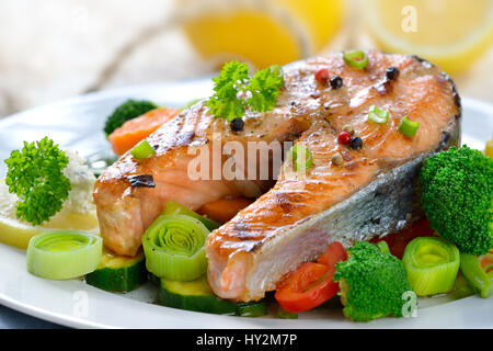 Gustosa grigliata bistecca di salmone su misto di verdure colorate, limoni e una rete da pesca in background Foto Stock