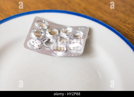 Set di pillole in una plastica e confezione giacente sul vassoio bianco con bordo blu Foto Stock