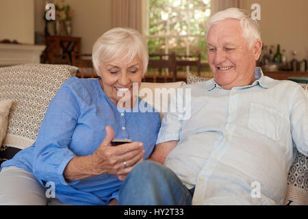Felice di anziani la lettura di messaggi di testo a casa sul loro lettino Foto Stock