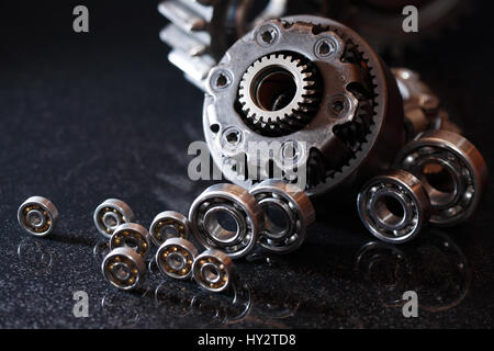 Concetto di macchinari. Set di vari ingranaggi e cuscinetti a sfera su sfondo scuro Foto Stock