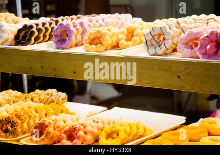 Visualizzazione delle deliziose paste in una pasticceria assortita con vetri colorati e gustosi bomboloni o krapfen con spruzzi e di ghiaccio su vassoi in un negozio coun Foto Stock