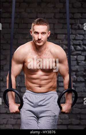 Crossfit core esercizio. Determinato uomo al lavoro in palestra di pull up con anelli di ginnastica per la resistenza Foto Stock