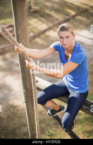 Montare determinata donna salendo verso il basso la fune durante il percorso ad ostacoli in boot camp Foto Stock