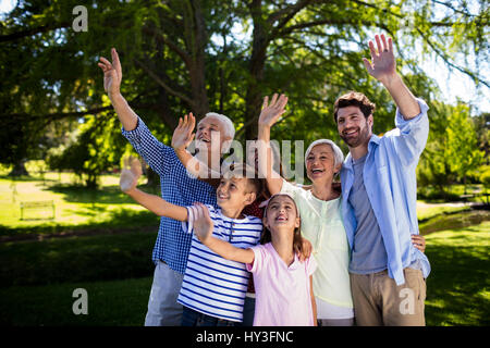 Felice multi generazione famiglia agitando la mano in aria al parco Foto Stock