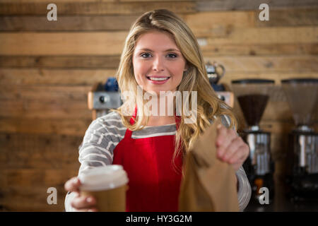 Ritratto di donna sorridente barista azienda tazza di caffè e sacchetto di carta nella caffetteria Foto Stock