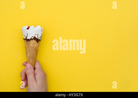 Mano azienda cono gelato su sfondo giallo Foto Stock