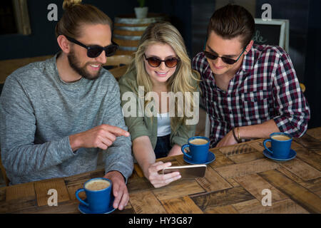 Sorridente giovani amici utilizzando smart phone a tavola in cafe Foto Stock