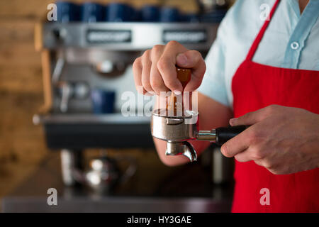 Sezione mediana del barista maschio utilizzando pressacaffè per premere il caffè macinato in portafilter in cafe Foto Stock