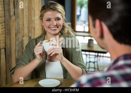 Sorridente giovane donna azienda tazza da caffè guardando un uomo in cafe Foto Stock