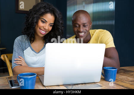 Sorridente coppia giovane utilizzando il portatile in tabella in coffee shop Foto Stock