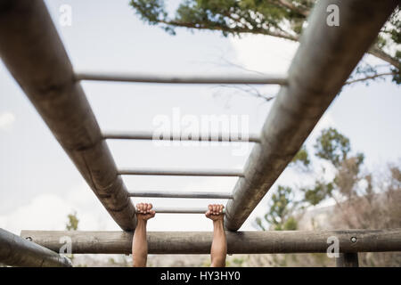 Montare l'uomo climbing Monkey bar durante la corsa a ostacoli in boot camp Foto Stock