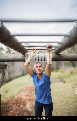 Montare donna climbing Monkey bar durante la corsa a ostacoli in boot camp Foto Stock