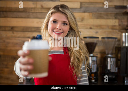 Ritratto di sorridente femmina giovane barista azienda monouso tazza di caffè nella caffetteria Foto Stock