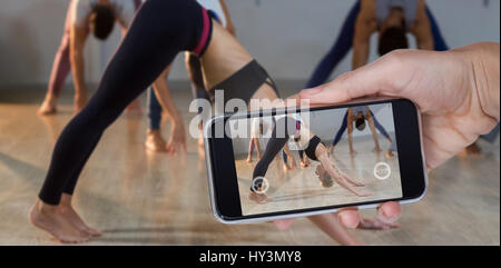 Mano che tiene il telefono cellulare contro uno sfondo bianco contro la donna di eseguire la posizione del Cane con la testa in giù pongono Foto Stock
