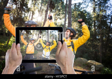 Ritagliato mano azienda digitale compressa contro il biker giovane con mountain bike in campagna Foto Stock