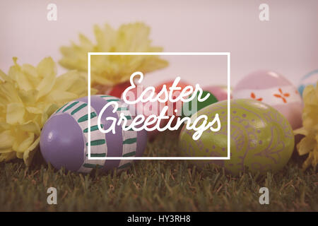 Saluto pasquale contro il dipinto di uova di Pasqua con i fiori di erba Foto Stock