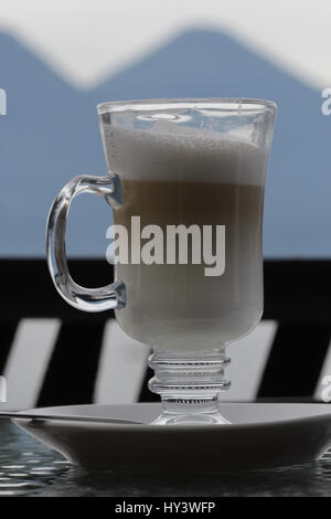 Vetro tazza di caffè servito in una piastra con le montagne in primo piano Foto Stock