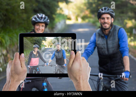 Ritagliato mano azienda digitale compressa contro il biker giovane con mountain bike su strada Foto Stock