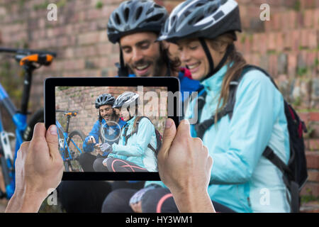Ritagliato mano azienda digitale compressa contro il biker giovane utilizzando il telefono cellulare Foto Stock