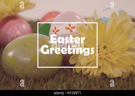 Saluto pasquale contro il dipinto di uova di Pasqua con i fiori di erba Foto Stock