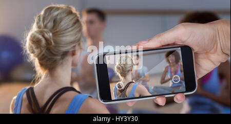 Mano che tiene il telefono cellulare contro uno sfondo bianco contro istruttore tenendo corsi di yoga Foto Stock