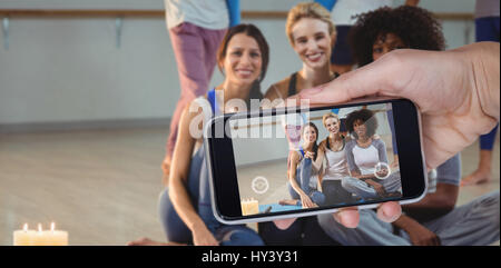 Mano che tiene il telefono cellulare contro uno sfondo bianco contro il ritratto di donna seduta sul tappetino di esercizio Foto Stock